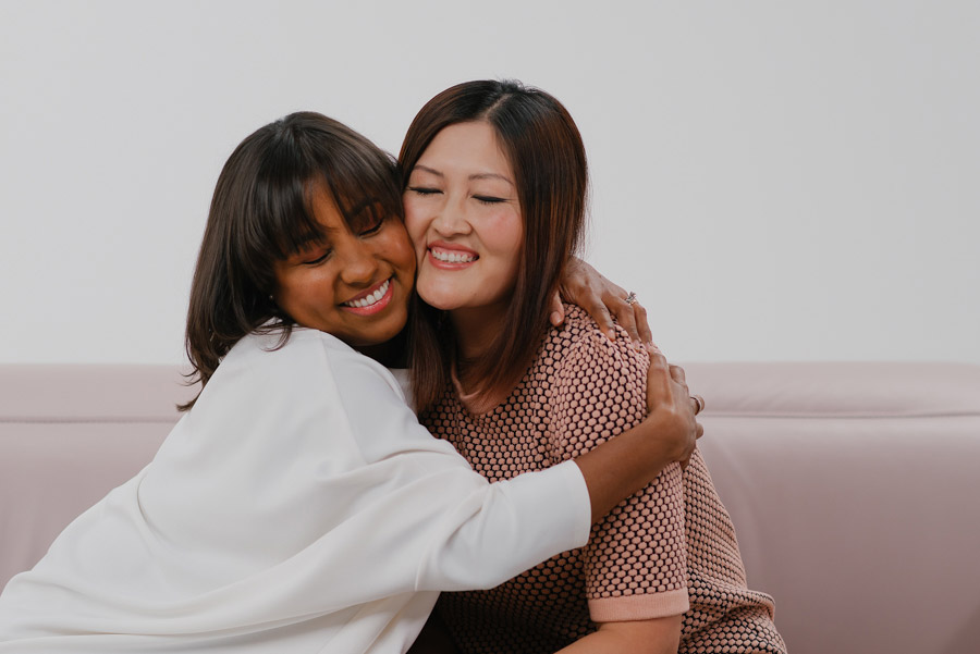 abbraccio tra donna cinese e donna brasiliana su divano Natuzzi in pelle rosa di design made in Italy